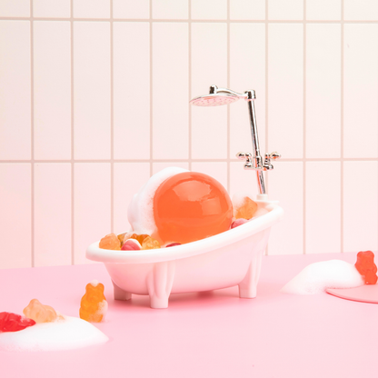 Naisture aqua jelly ball cleanser orange jelly sphere resting in mini bathtub with foam and gummy bears