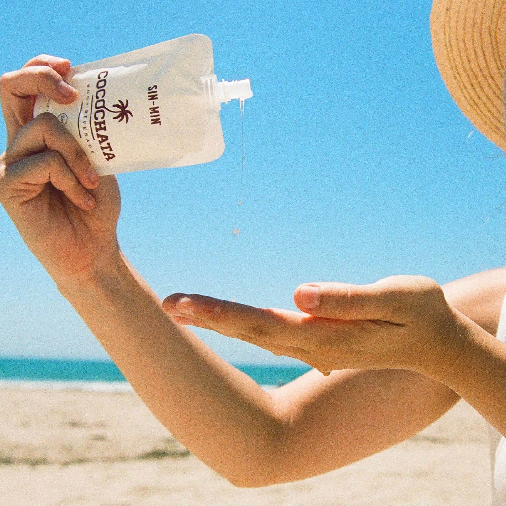 SIN-MIN coconut oil cinnamon body lotion being poured from a pouch onto hand at the beach