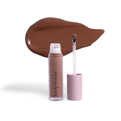 Dominique Cosmetics concealer in a matte brown shade with applicator wand and swatch on white background