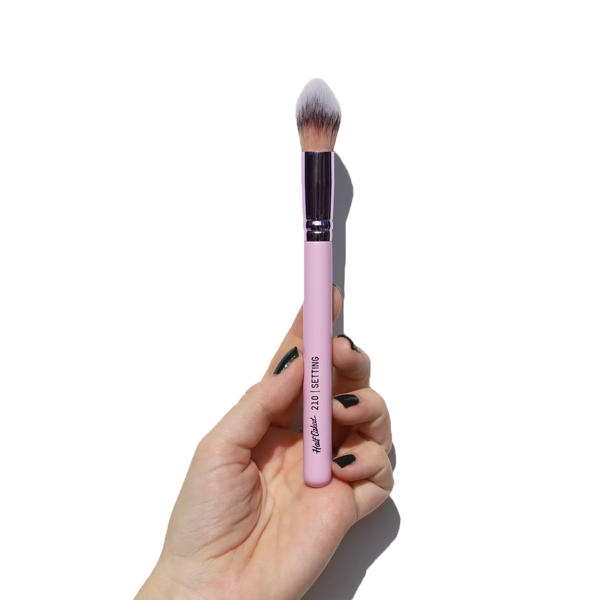 Hand holding Half Caked 210 Setting Brush with pink handle and soft bristles for face makeup