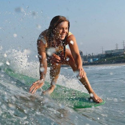 Smiling woman surfing on a green board at the beach protected by indie sunscreen stick