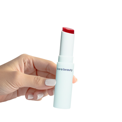 Kara Beauty strawberry gloss stick in white tube held in hand showing red glossy balm tip