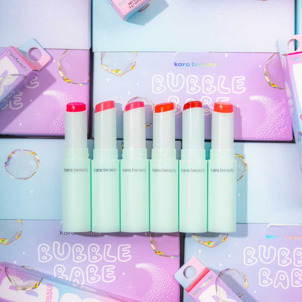 Six Kara Beauty strawberry gloss stick lip balms in mint tubes with mixed pink and coral shades on Bubble Babe boxes