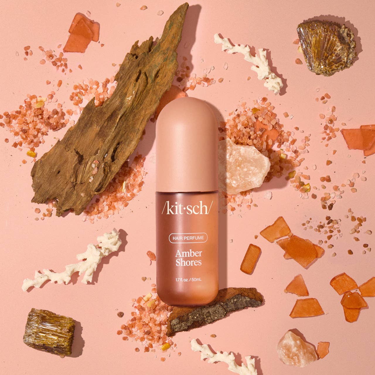 Amber hair perfume by Innovate the Label in a pink bottle surrounded by natural amber and wood elements