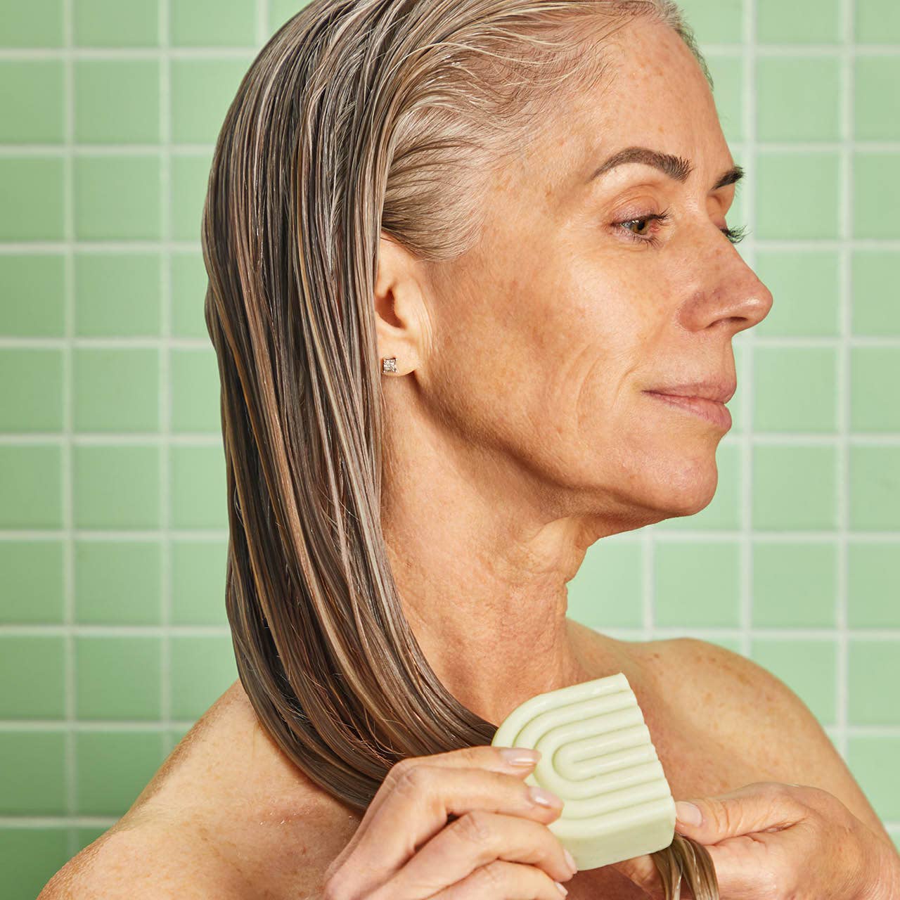 Innovate the Label anti dandruff conditioner bar applied to wet gray hair by woman in green tiled shower
