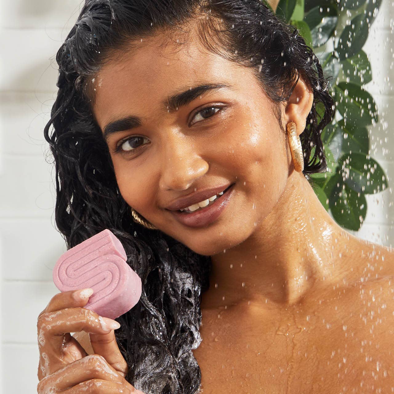 Woman holding a pink castor oil shampoo bar while washing wet hair in the shower