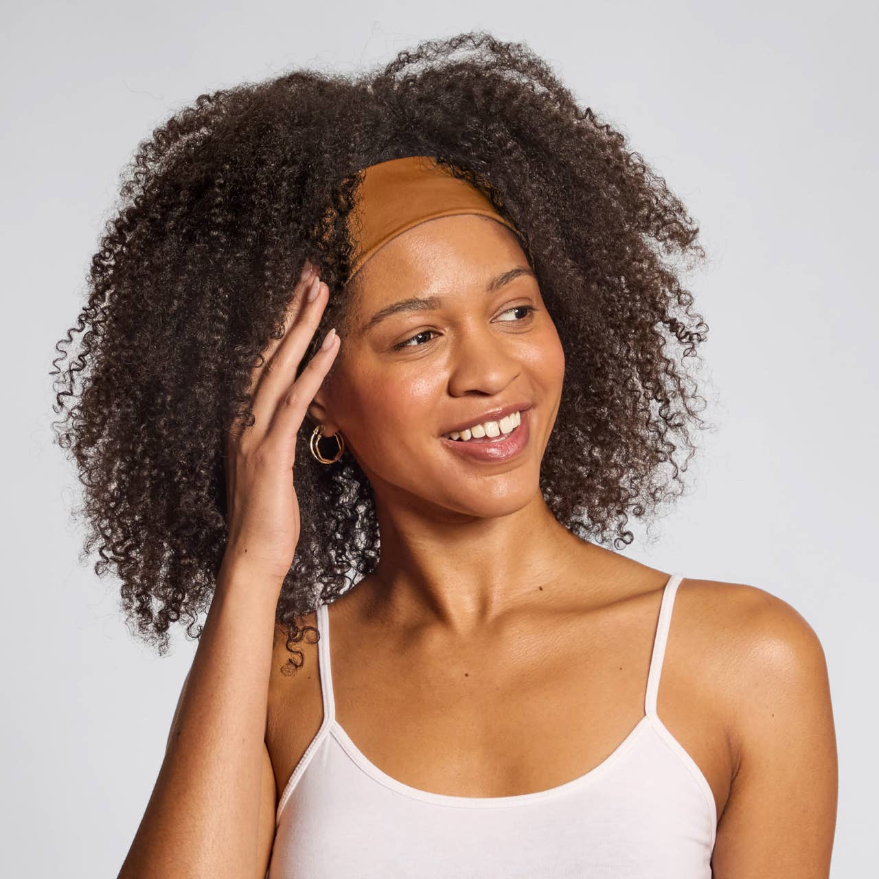 Smiling woman with natural curly hair wearing a brown eco-friendly workout headbands and white tank top