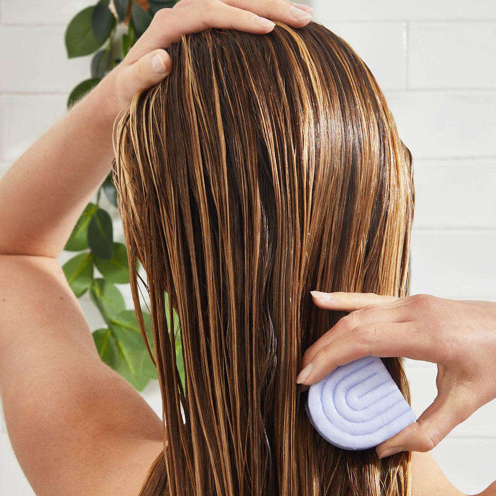 Woman applying purple toning conditioner bar to wet blonde hair for color maintenance
