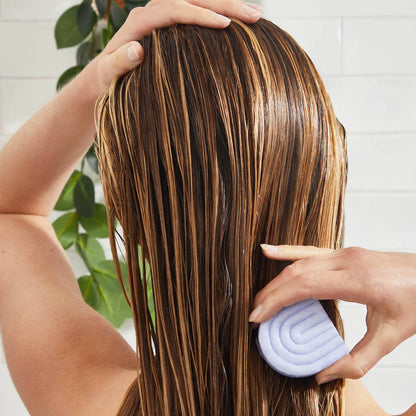 Woman applying purple toning conditioner bar to wet blonde hair for color maintenance