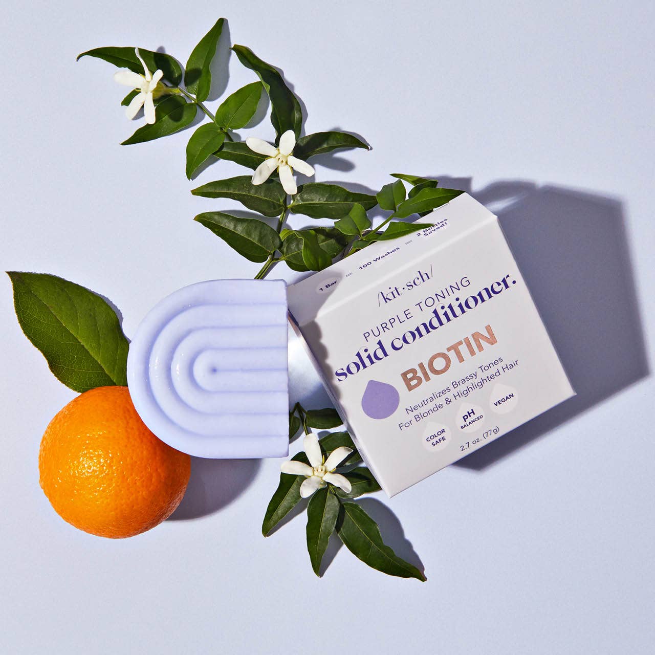 Innovate the Label purple toning conditioner bar with box, placed next to orange and green leaves with white flowers