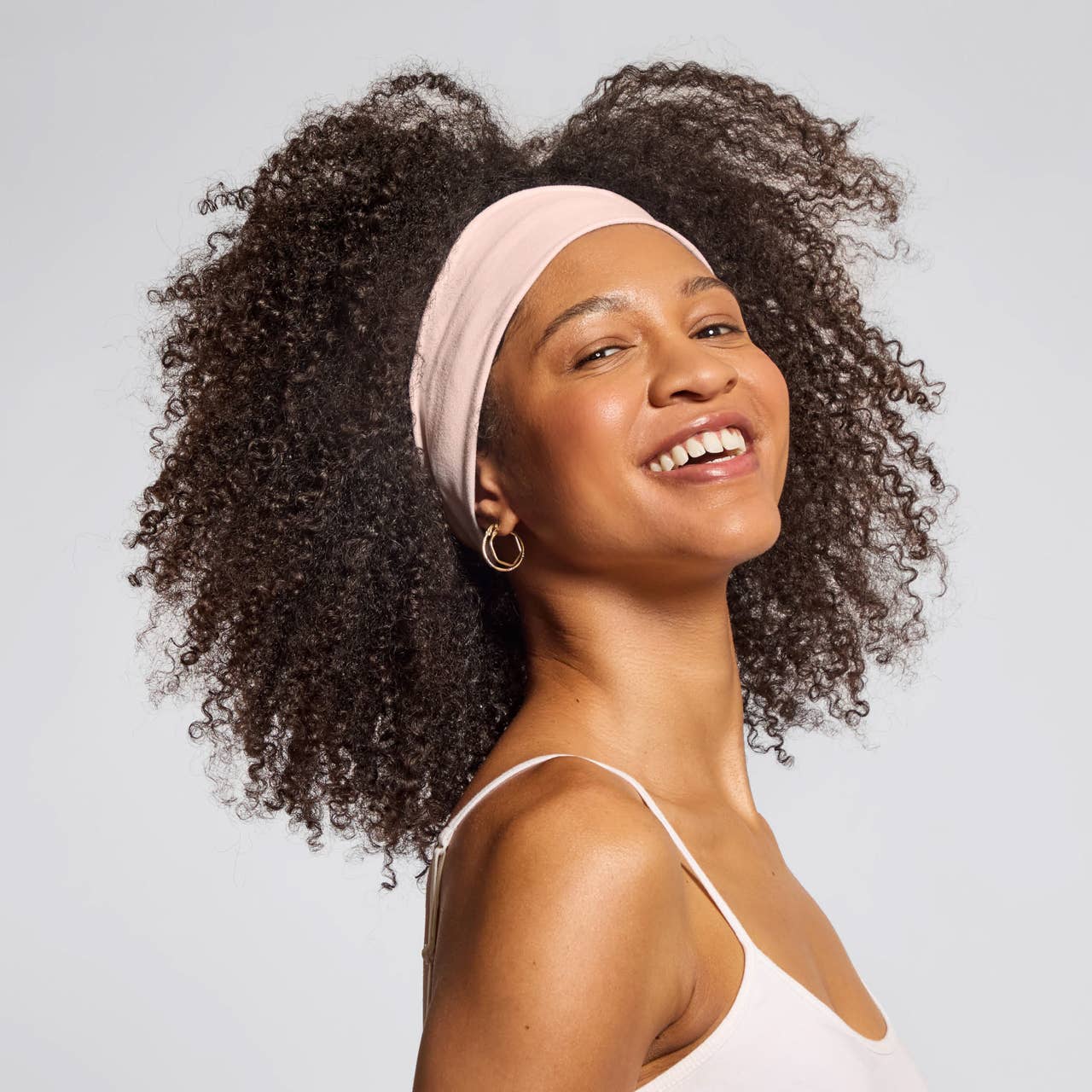 Smiling woman with natural curls wearing wide soft pink eco-friendly workout headbands for sweat control