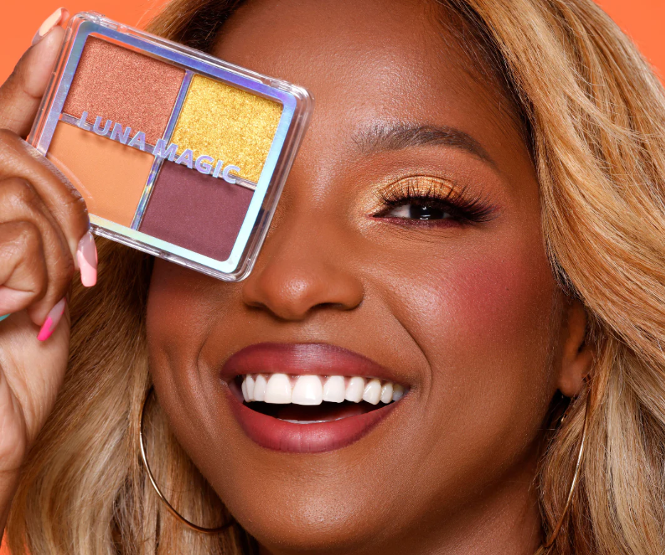 Smiling woman holding Luna Magic Desert Heat Eyeshadow Quad showcasing warm gold and brown shades