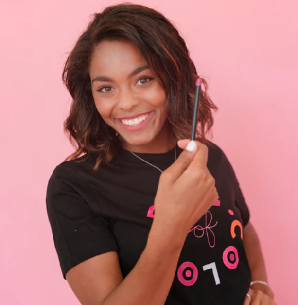 Smiling woman holding a creamy lip liner crayon from Innovate the Label Beauty Bundles against a pink background
