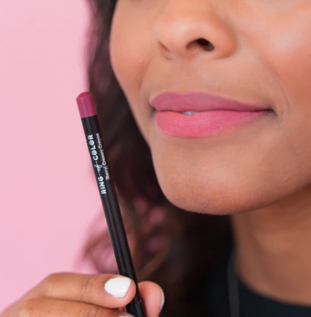 Creamy lip liner crayon in deep pink shade held near lips with matching pink lipstick