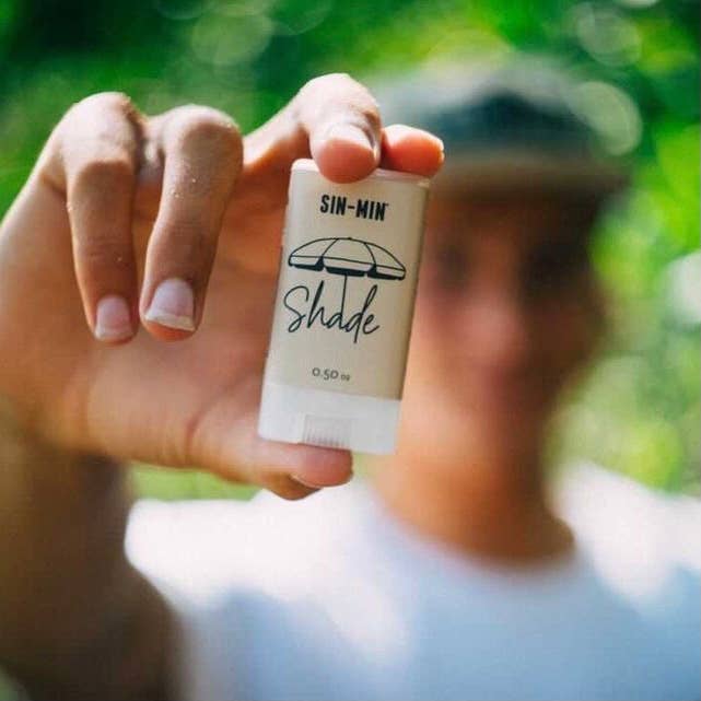 SIN-MIN indie sunscreen stick Shade held outdoors with blurred natural green background