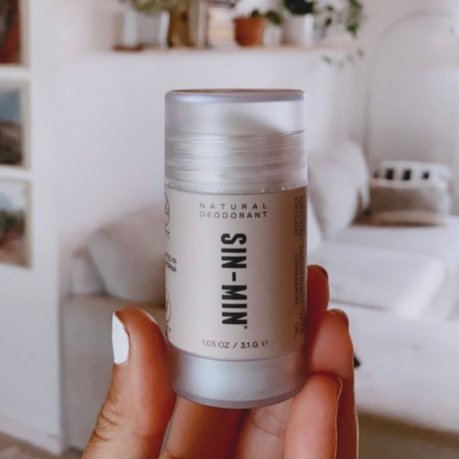 SIN-MIN natural travel size deodorant held in hand with a neutral indoor background