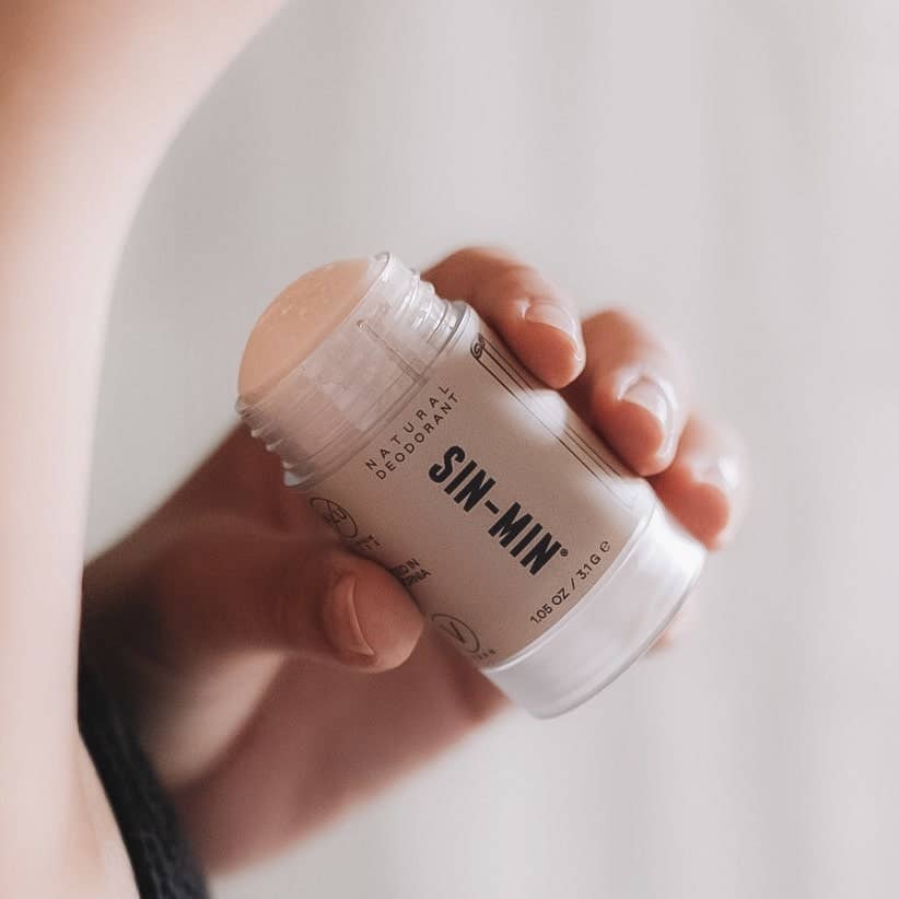 SIN-MIN natural travel size deodorant stick held in hand with beige background