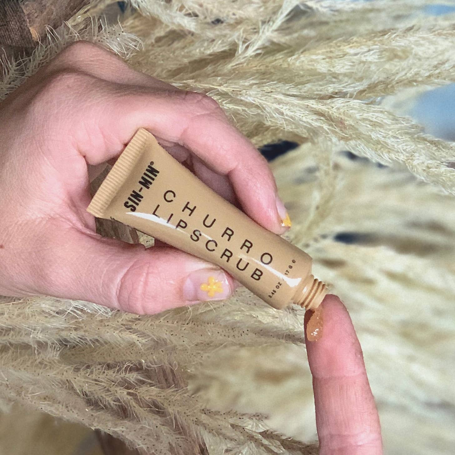 SIN-MIN vegan lip scrub tube with brown exfoliating scrub on fingertip against natural background