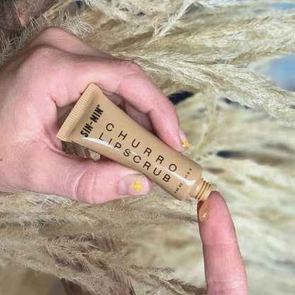SIN-MIN vegan lip scrub tube with brown exfoliating scrub on fingertip against natural background