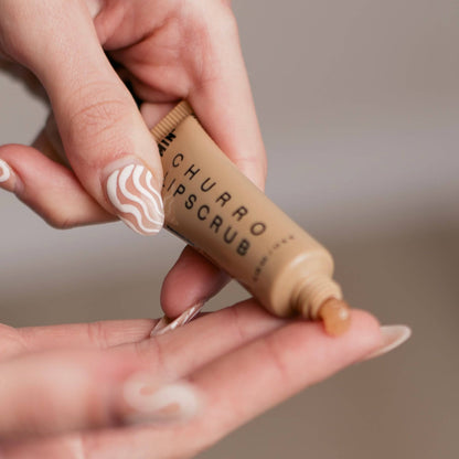SIN-MIN vegan lip scrub in a small tube being dispensed onto a finger with artistic nail design